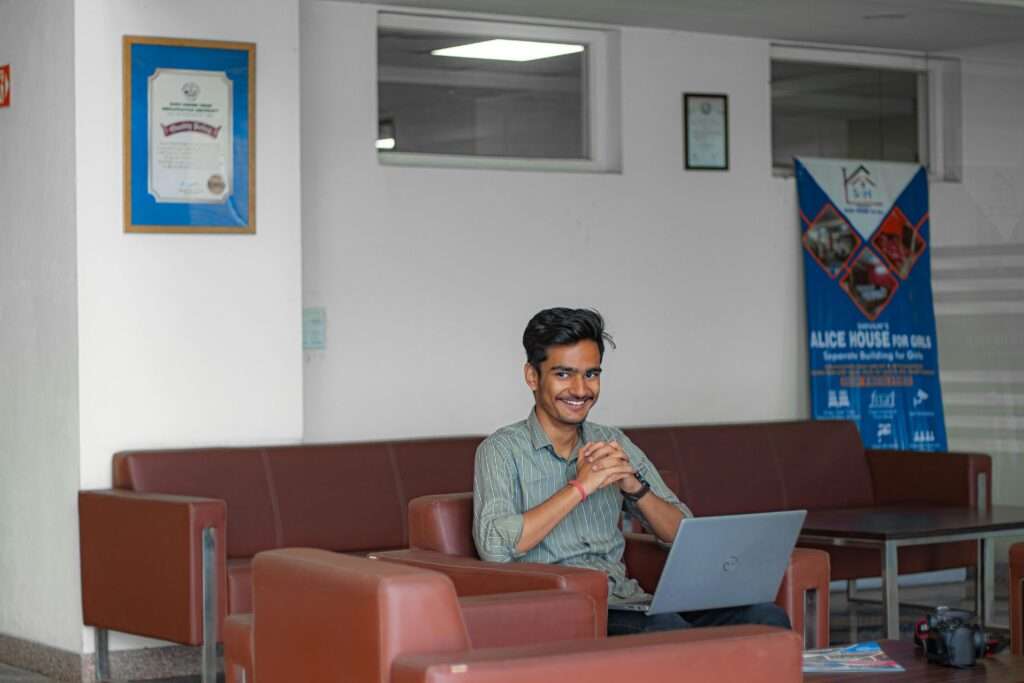 Smiling young adult sitting with laptop in a modern office lounge, focusing on work.